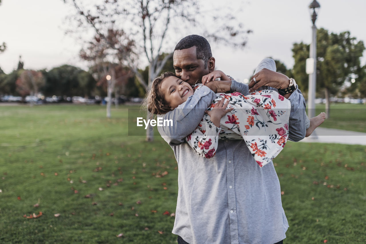 Happy father holding cute girl at park playground at dusk