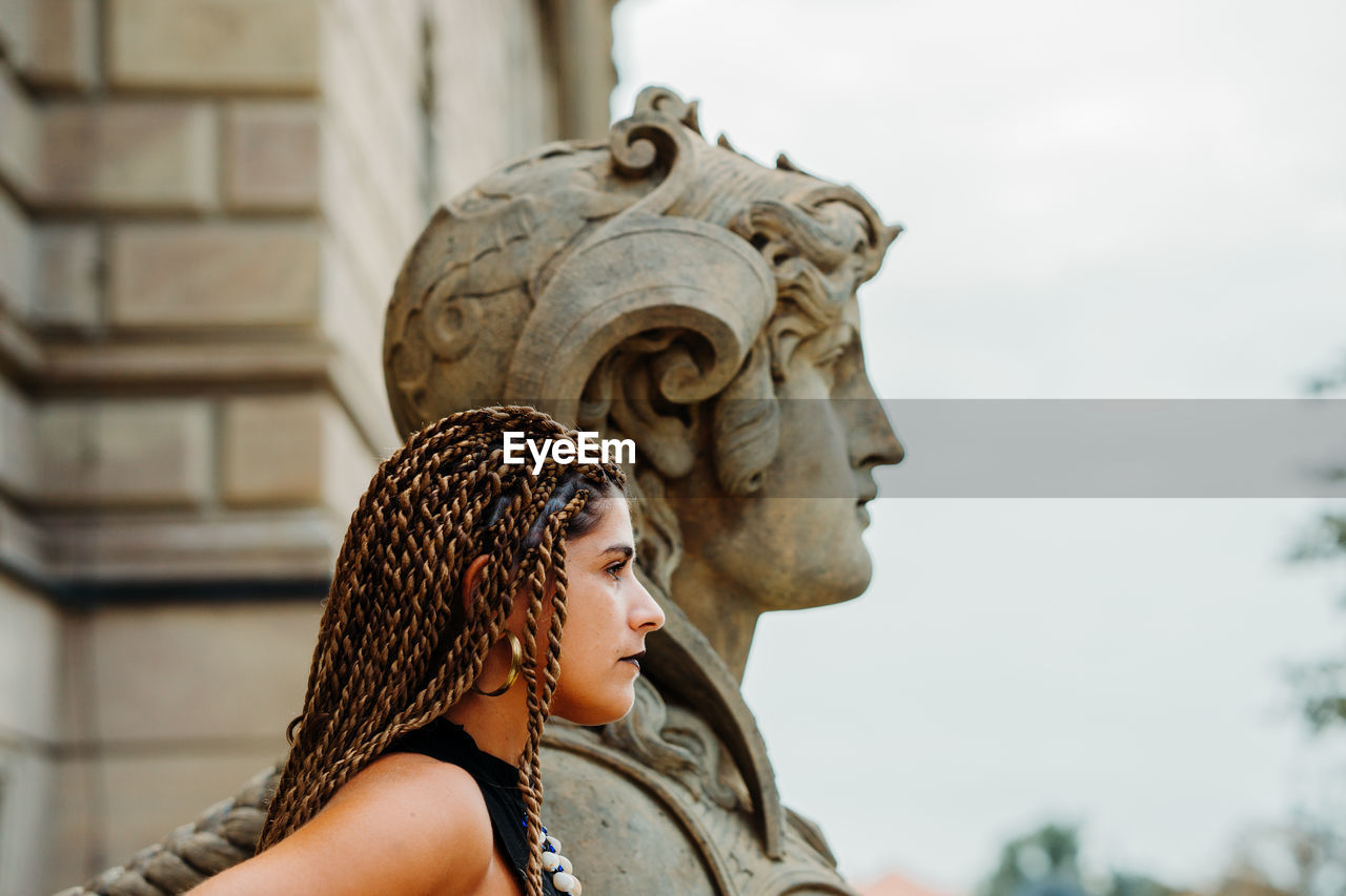 Close-up of woman looking away while standing by statue against historic building