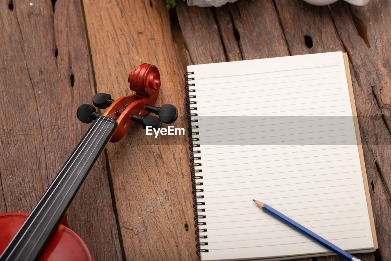 High angle view of violin by spiral notebook and pencil on table