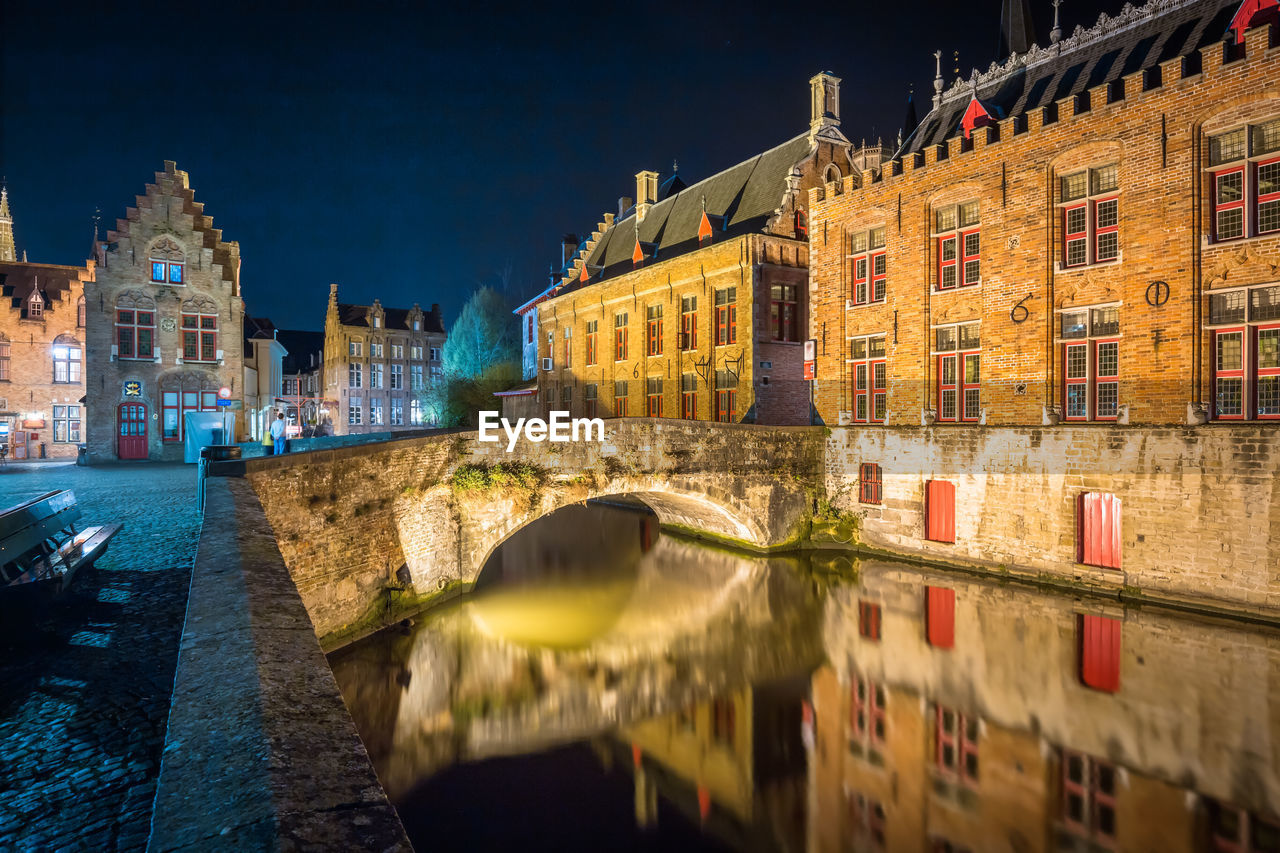 Canal by illuminated buildings in city at night