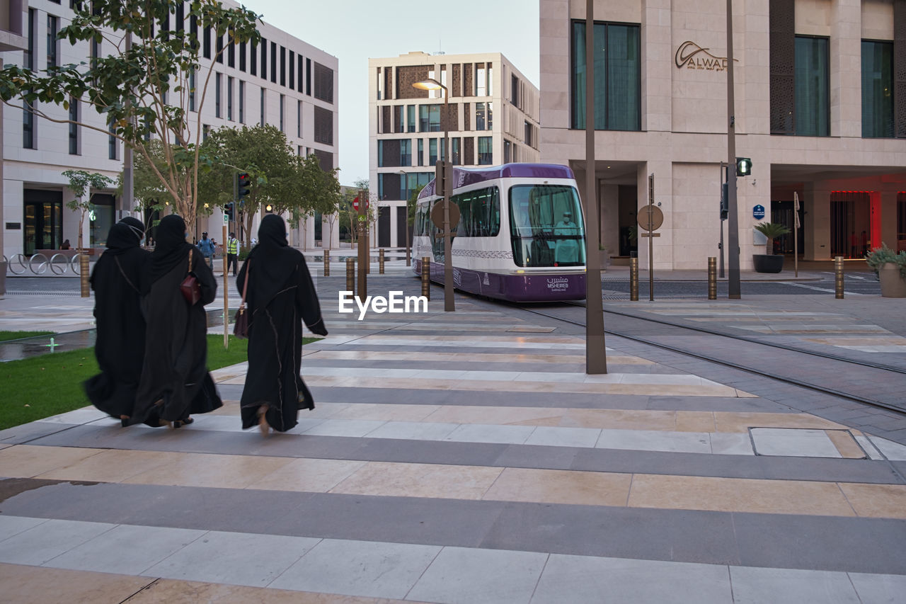 REAR VIEW OF PEOPLE WALKING ON STREET AGAINST BUILDINGS