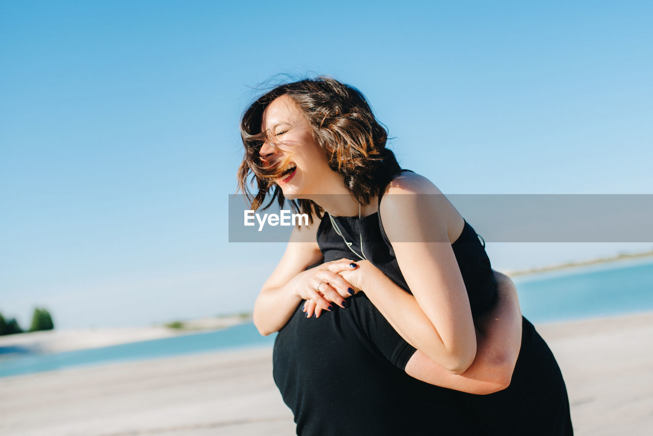 WOMAN STANDING ON BEACH AGAINST SKY