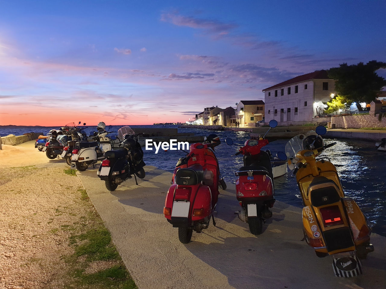 Vespa scooters parked in a row by the sea against sunset sky
