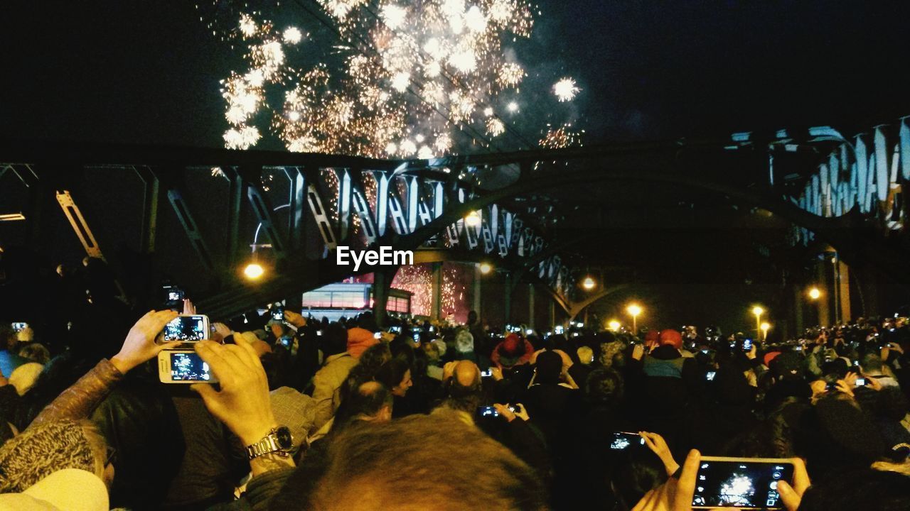 People photographing firework display on bridge at night