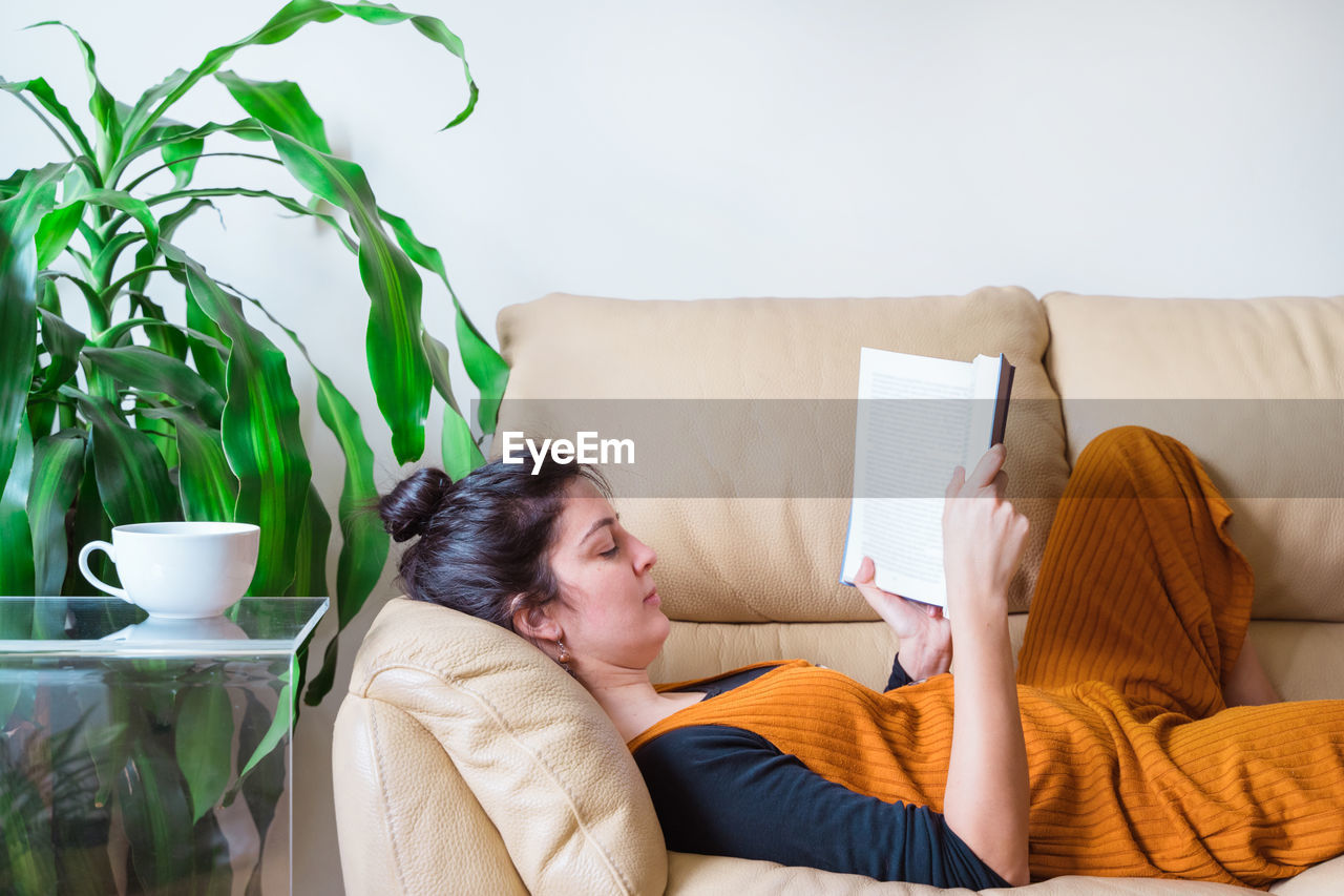 Woman reading book while sitting on sofa at home