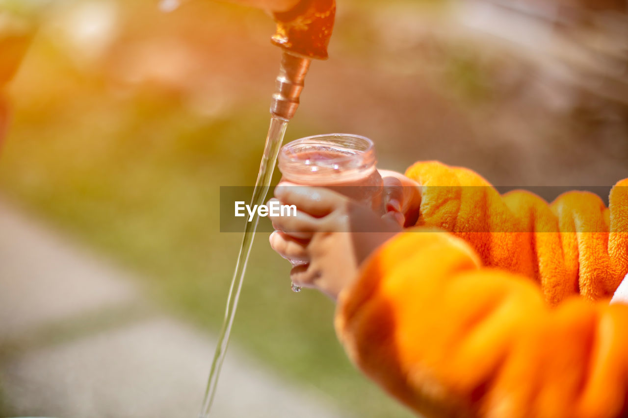 Faceless child fill the glass with water in water tap outdoor person