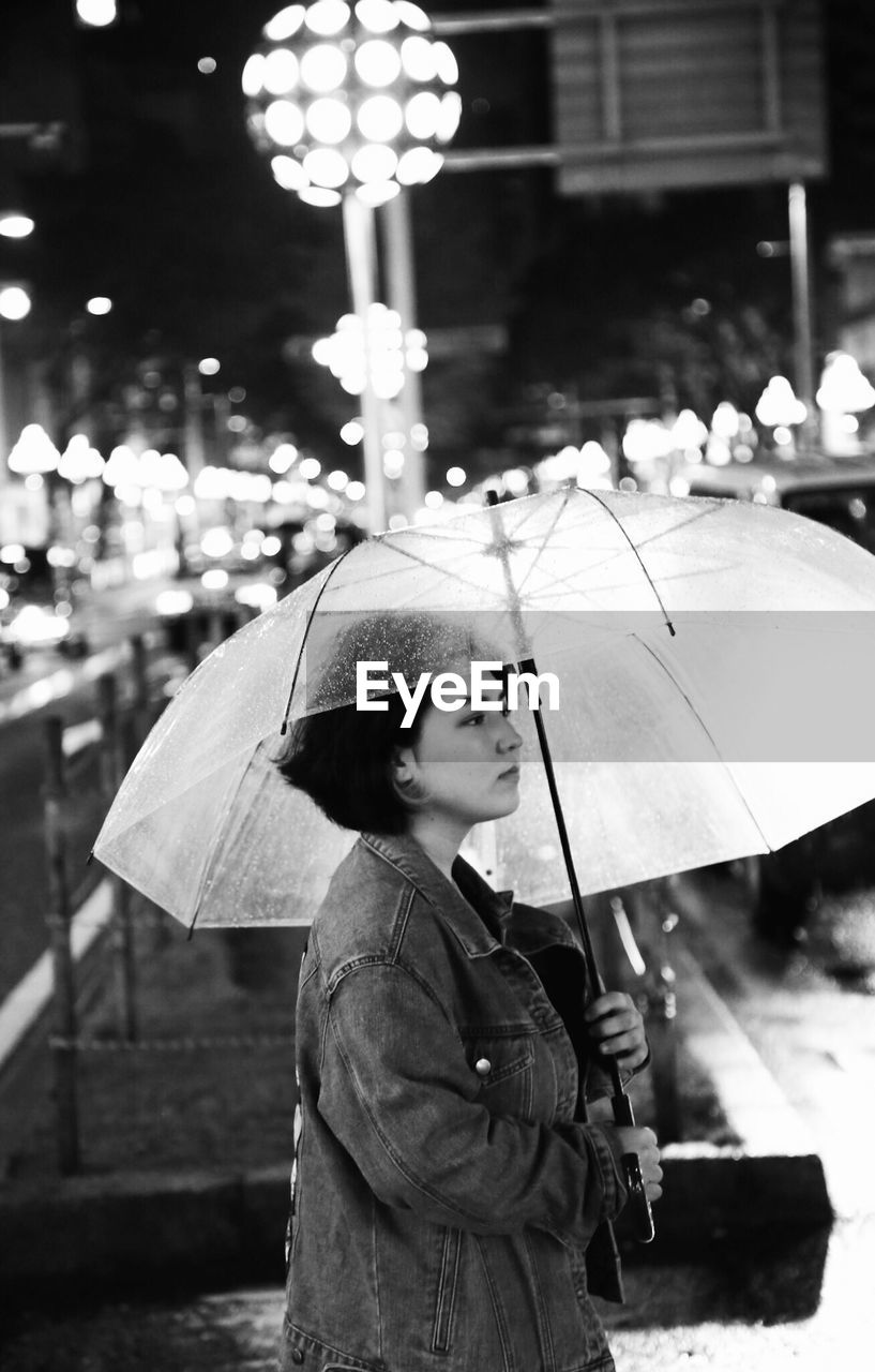 Young woman with umbrella in city at night during rain