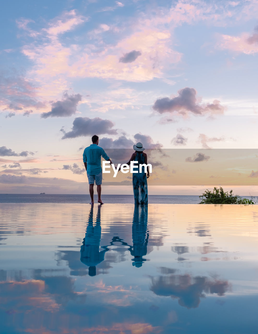 rear view of woman standing on shore at beach against sky during sunset