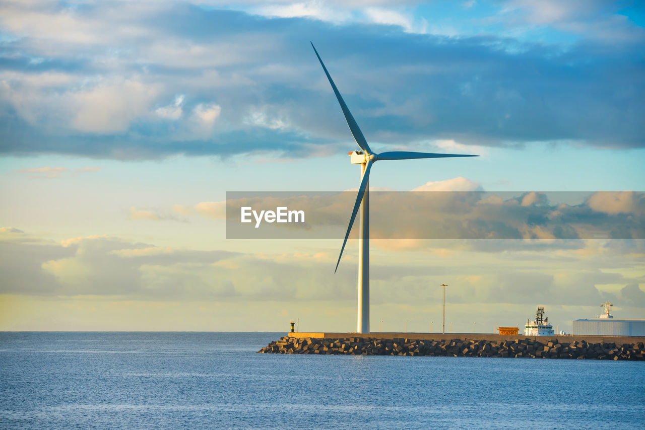 View of sea bay and large windmill at edge of stone breakwater