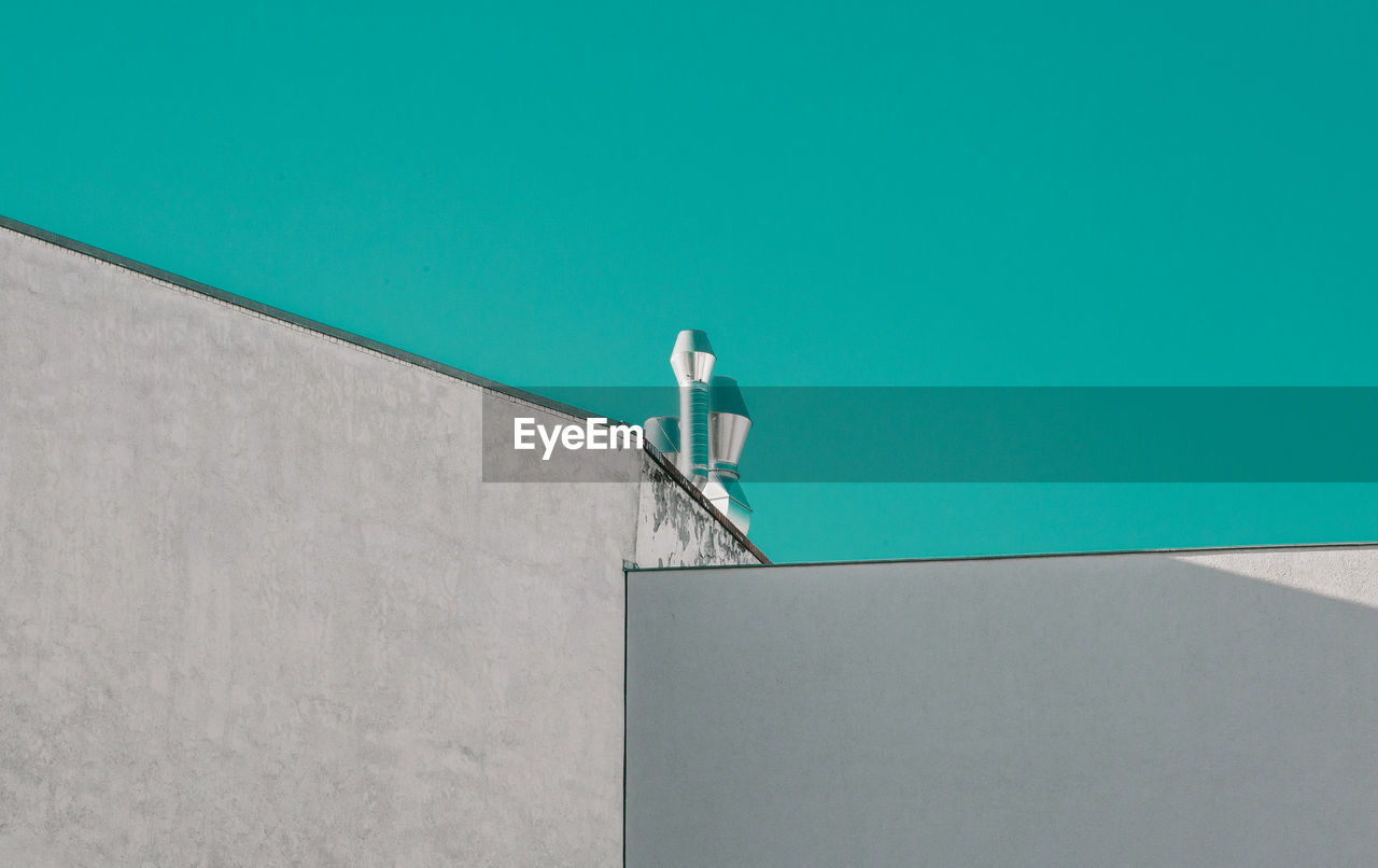 Low angle view of silver chimneys on building against clear turquoise sky