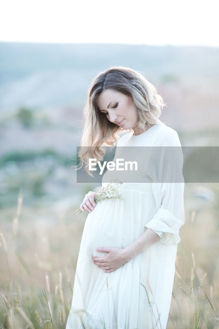 Pregnant woman holding belly standing on field