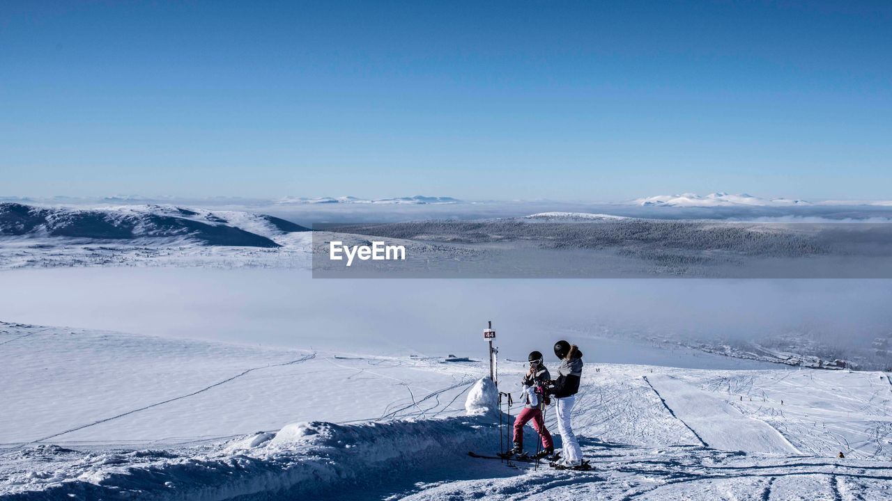 PEOPLE SKIING BY SNOWCAPPED MOUNTAIN AGAINST SKY