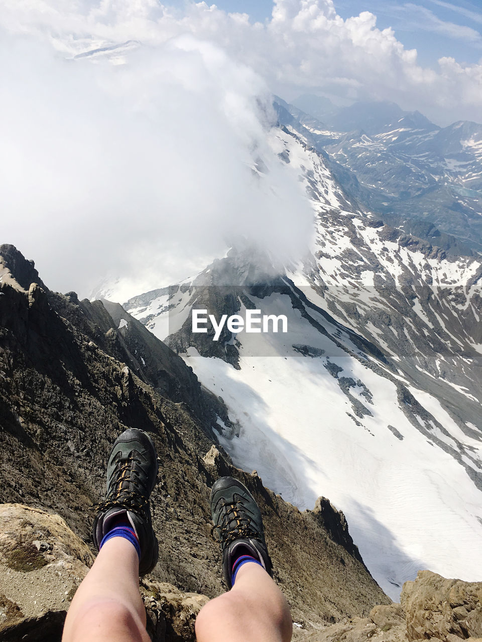 LOW SECTION OF PERSON ON SNOWCAPPED MOUNTAIN AGAINST SKY