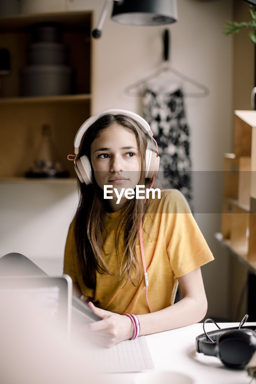 Girl wearing headphones sitting at desk while looking away