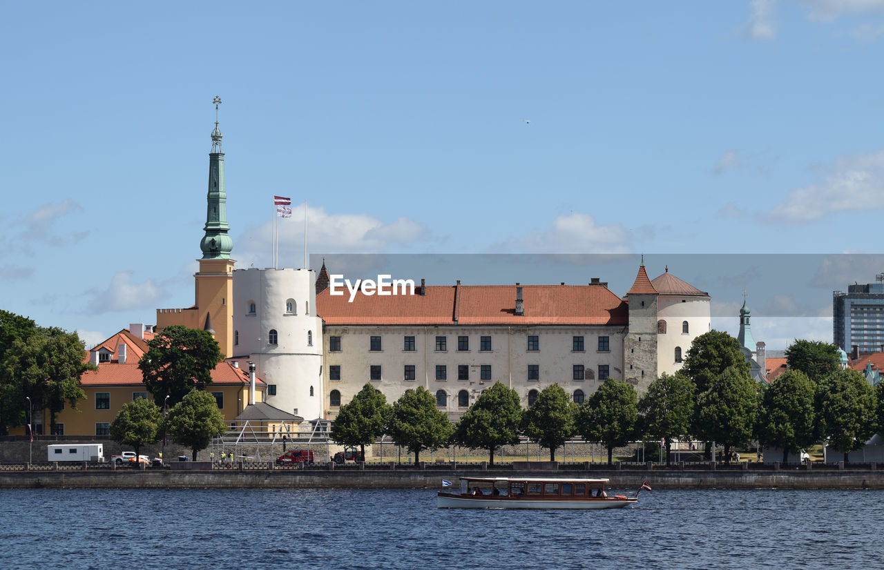 Buildings by river against sky in city