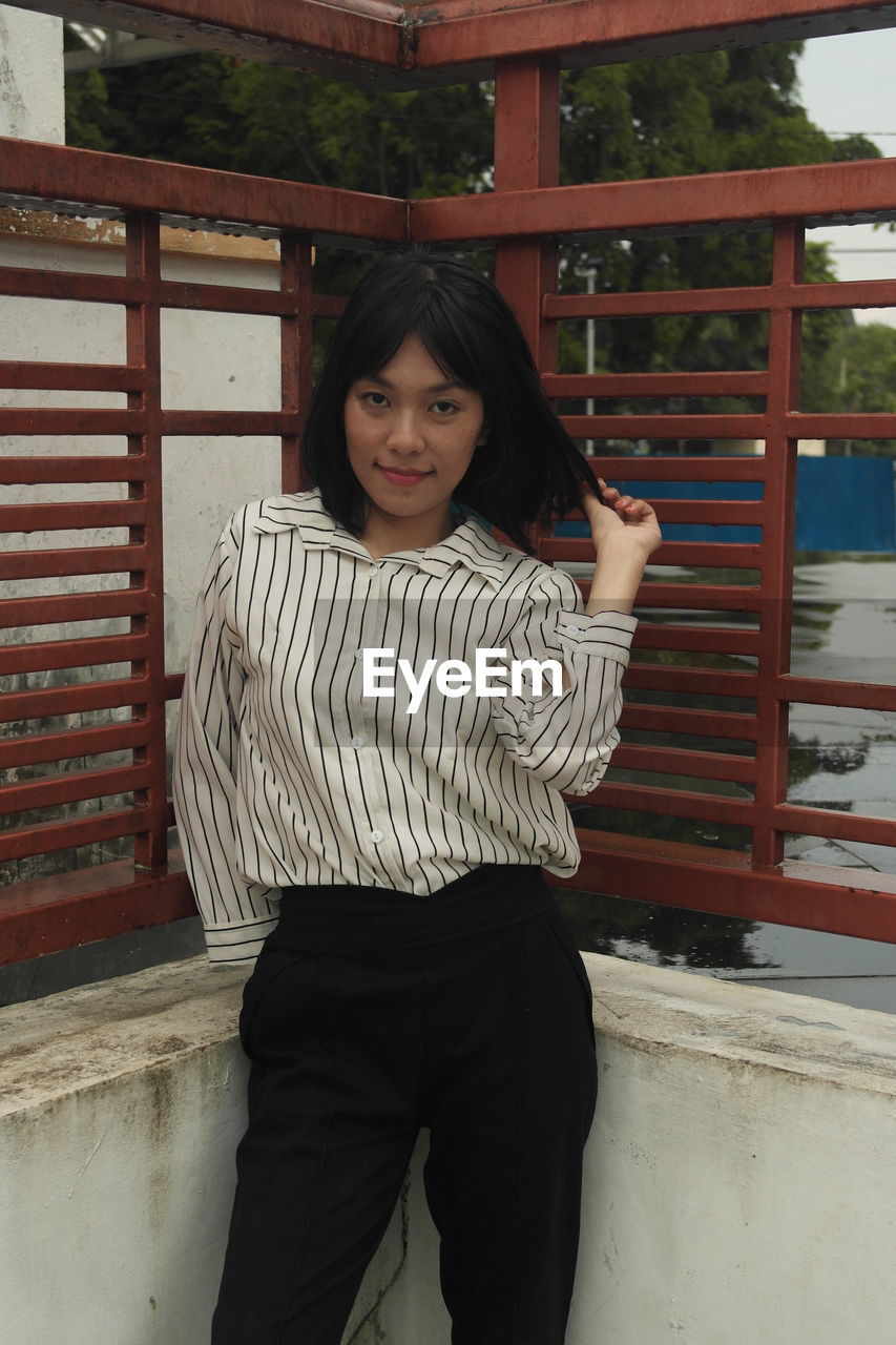 Portrait of young woman standing by railing