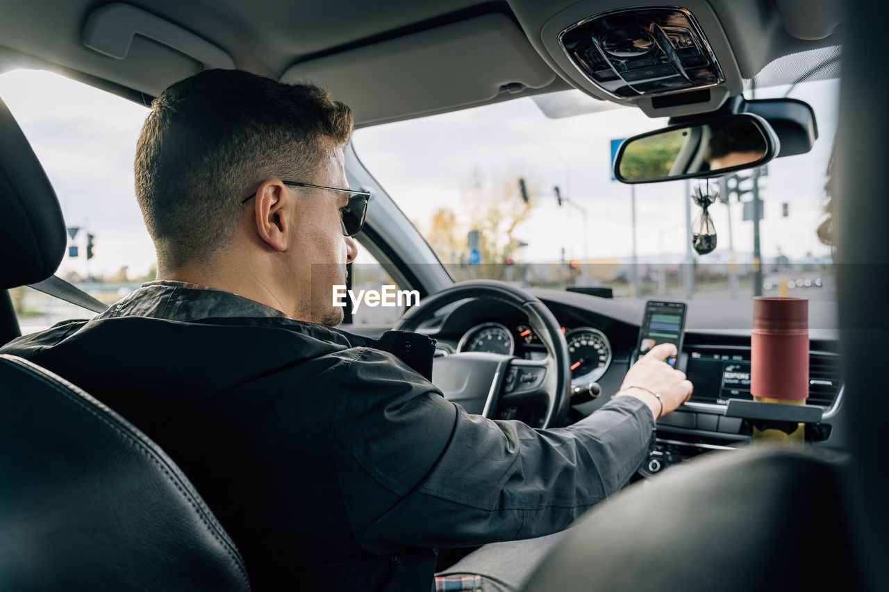 A man uses a smartphone installed in the holder while driving a car