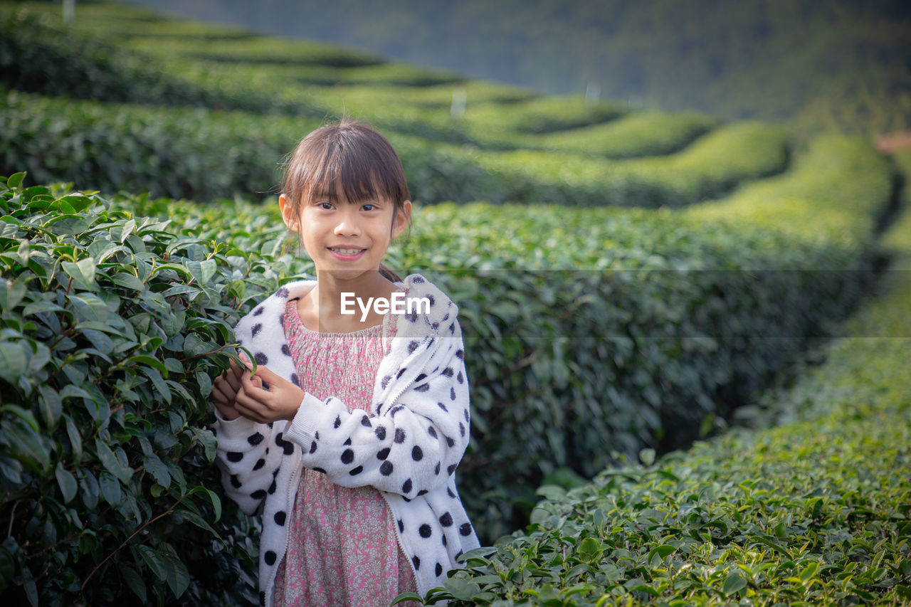 SMILING YOUNG WOMAN STANDING IN FIELD