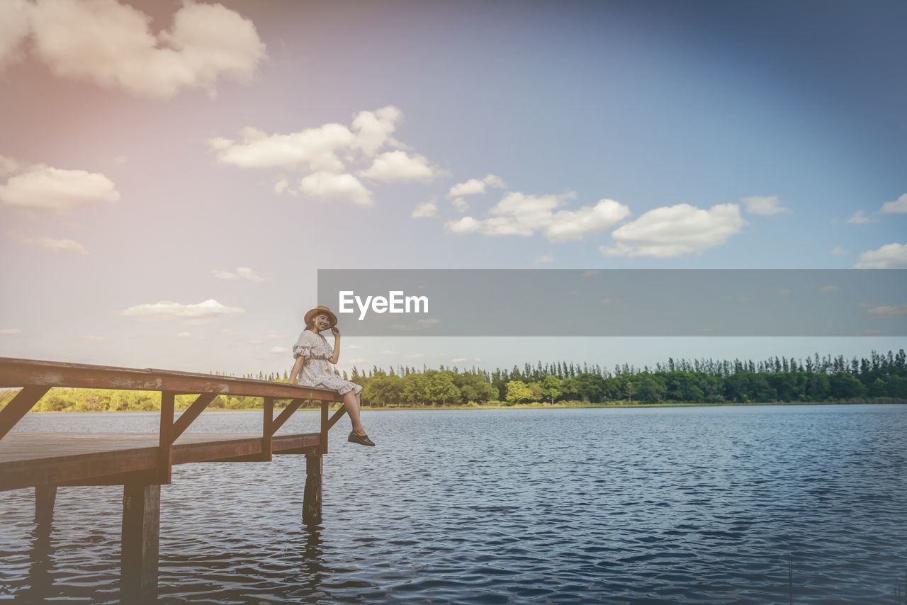 WOMAN SITTING AT LAKE AGAINST SKY