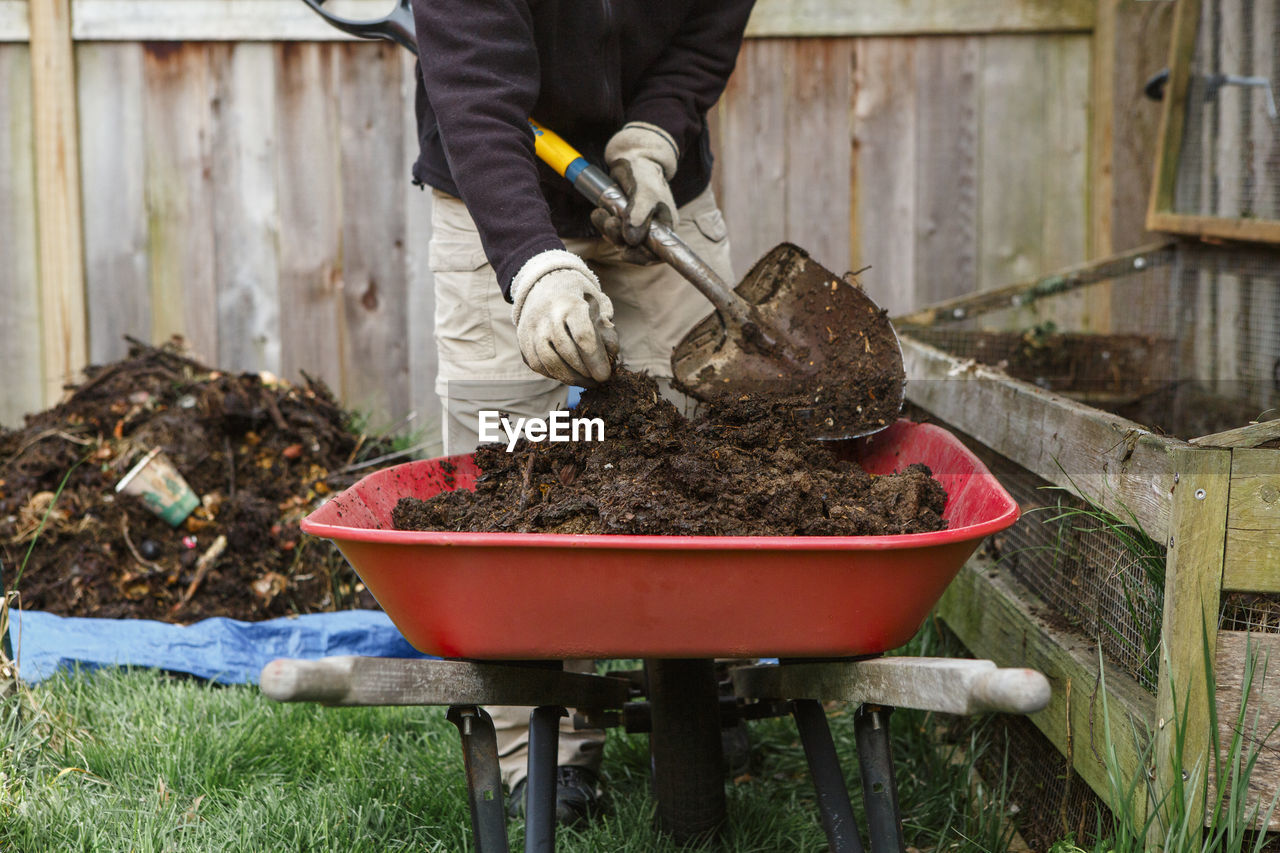 Bottom-half of person shoveling compost into red wheelbarrow in garden