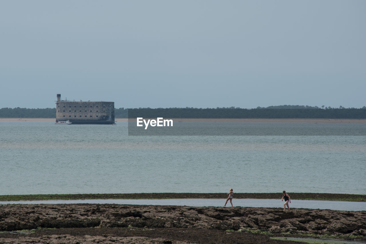 PEOPLE STANDING ON SHORE AGAINST CLEAR SKY