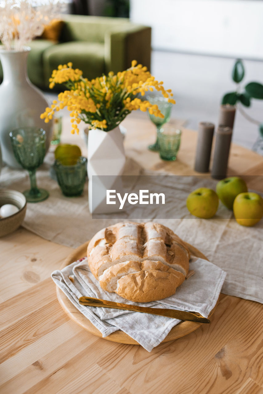 A loaf of fresh bread on the breakfast table, mimosa flowers in a vase