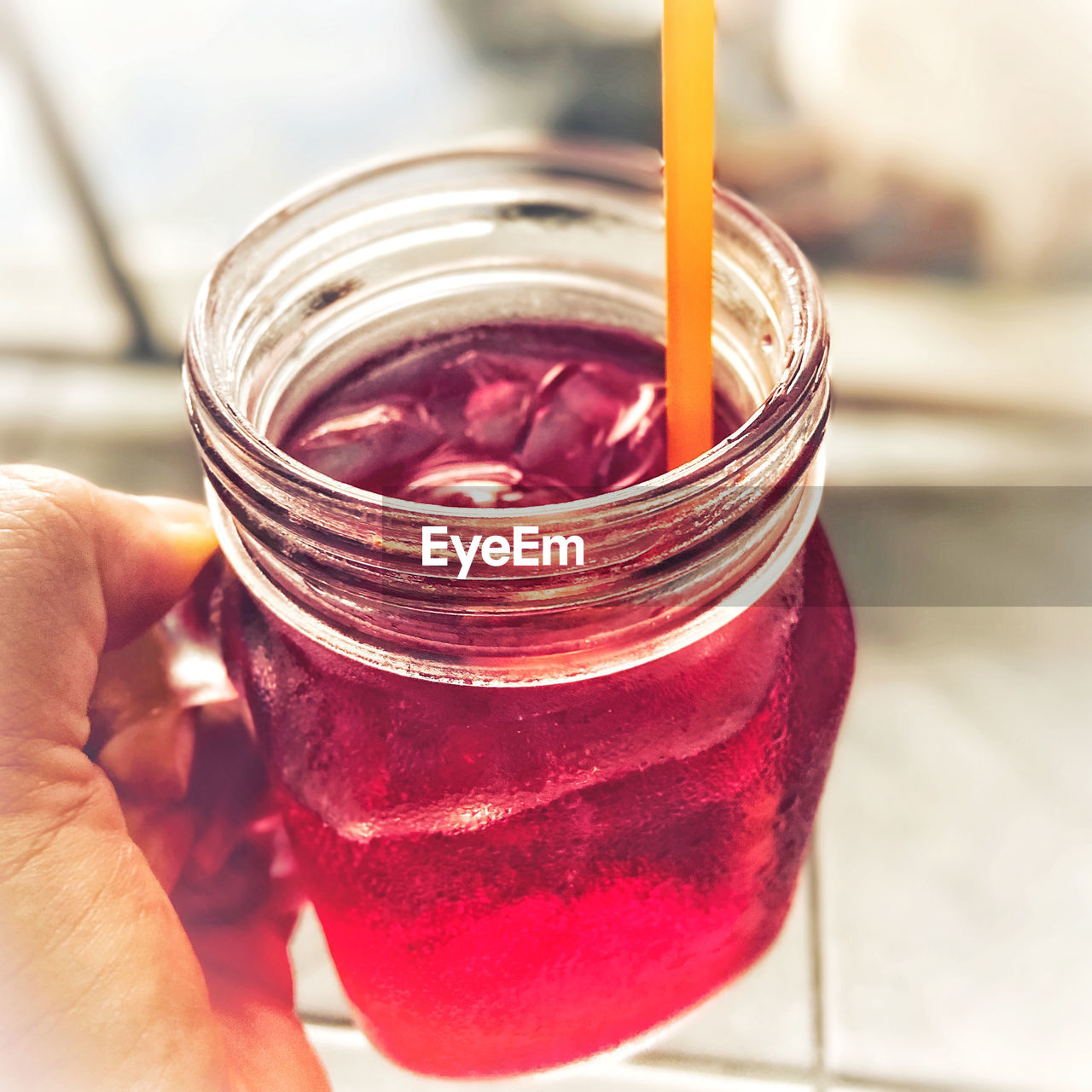 CLOSE-UP OF HAND HOLDING GLASS JAR WITH STRAW