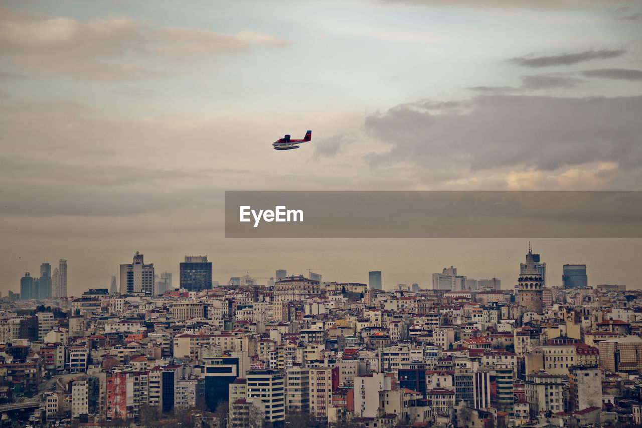 Airplane flying over cityscape against sky