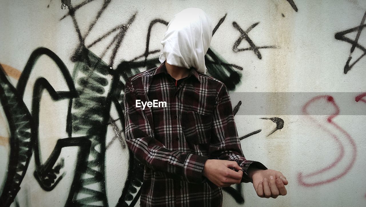 Man with face covered by cloth against graffiti wall