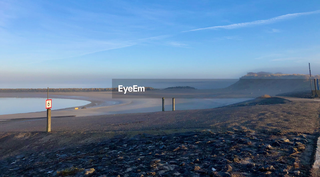 Road sign on misty coast landscape against blue sky