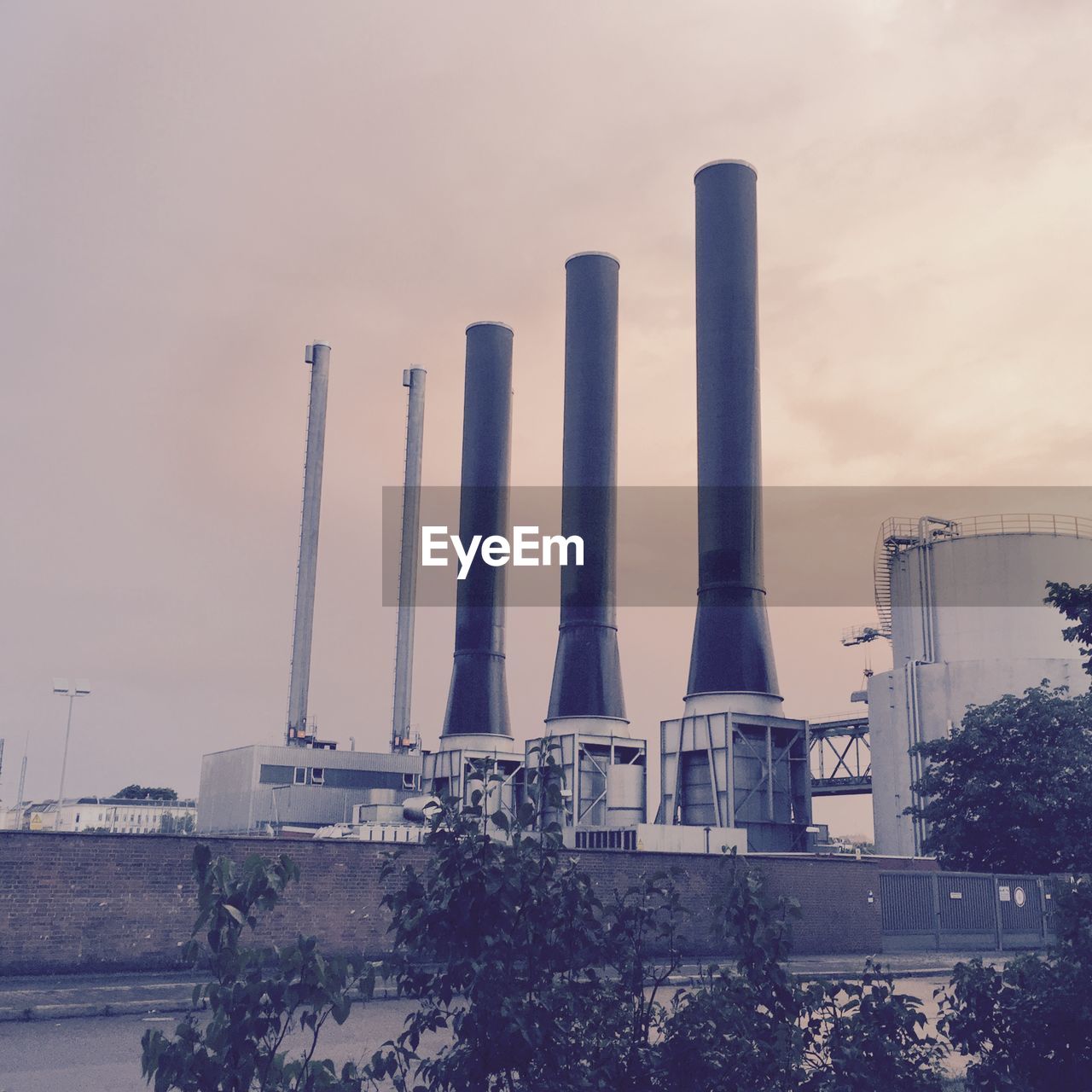 Low angle view of smoke stacks on factory against cloudy sky