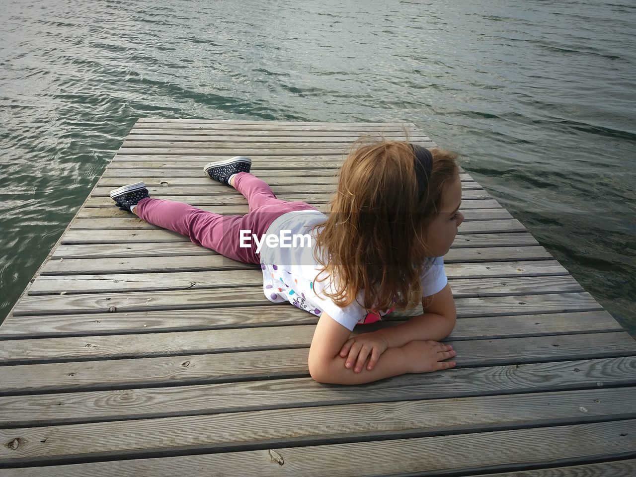 Girl lying on pier over lake