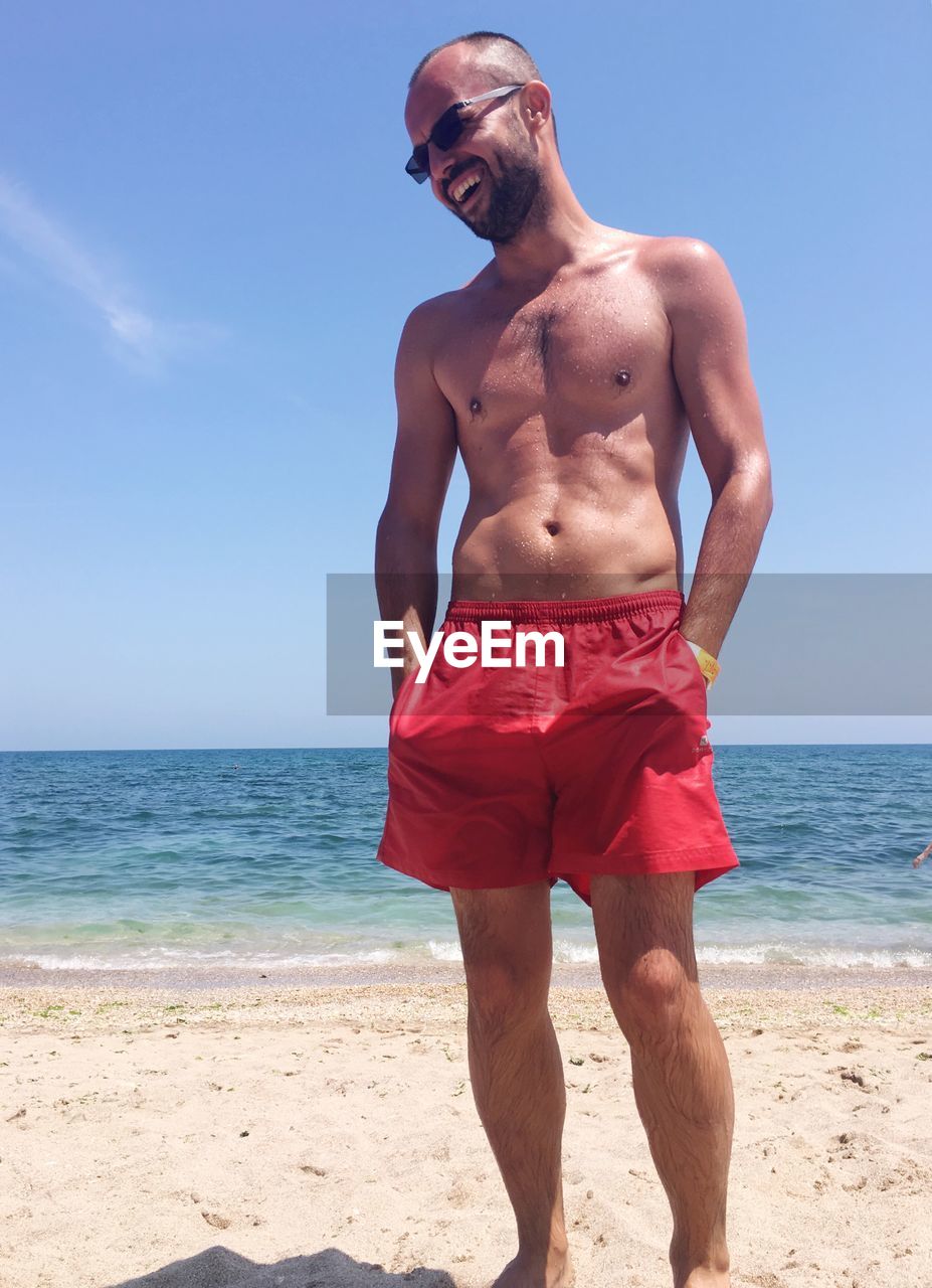 Shirtless man standing at beach against sky