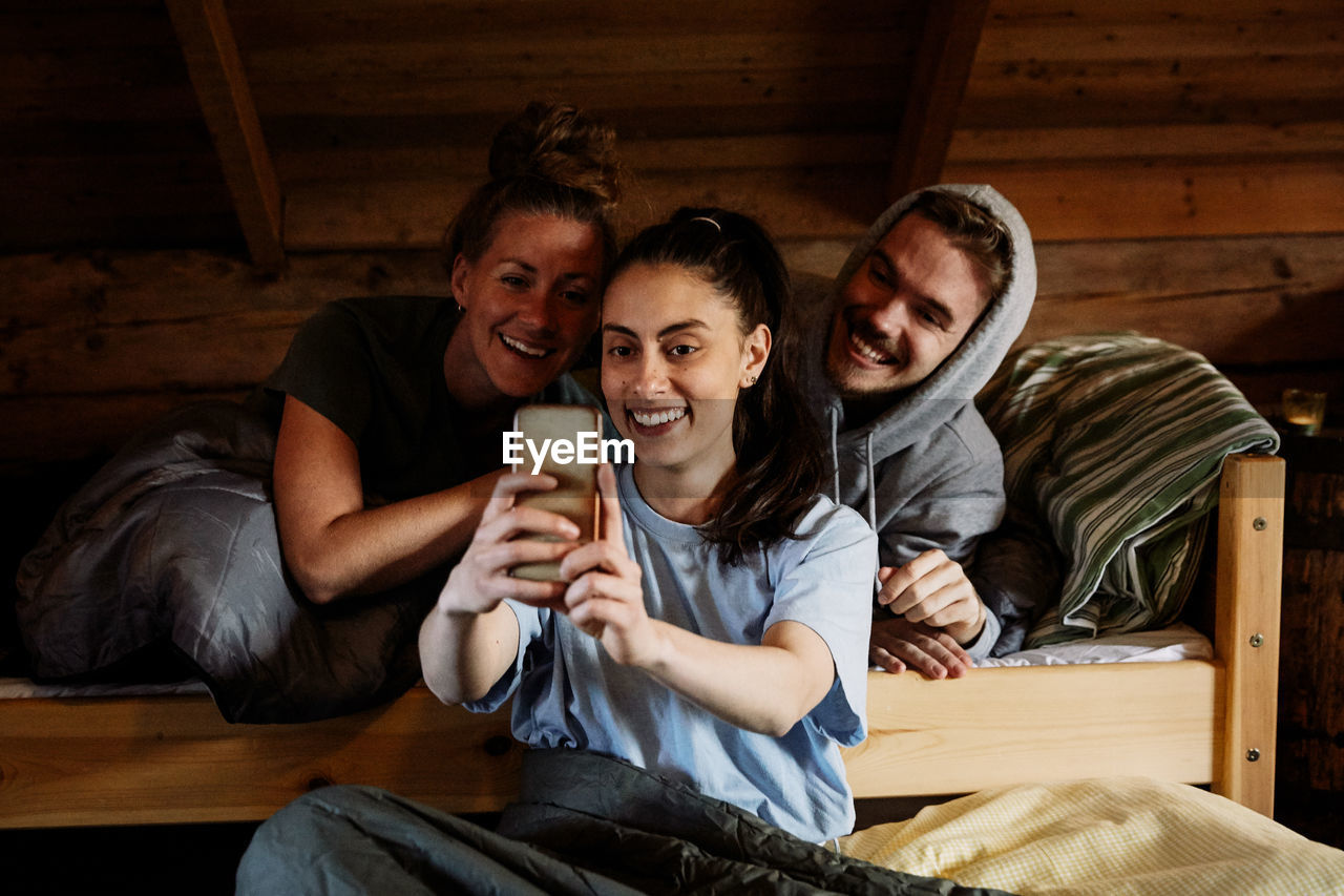 Smiling young woman taking selfie with enjoying with friends in cottage