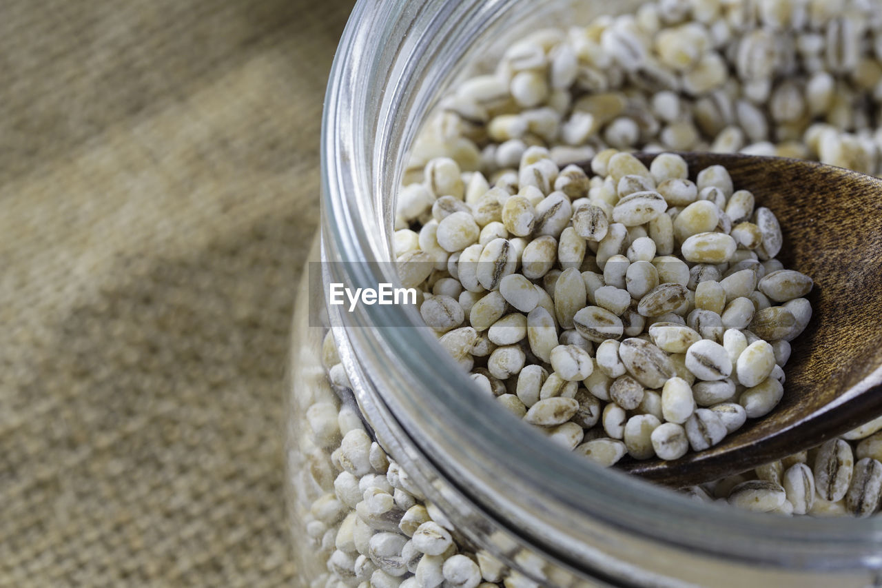 A close up on a raw barley wheat around the glass cointain water barley over brown sack.