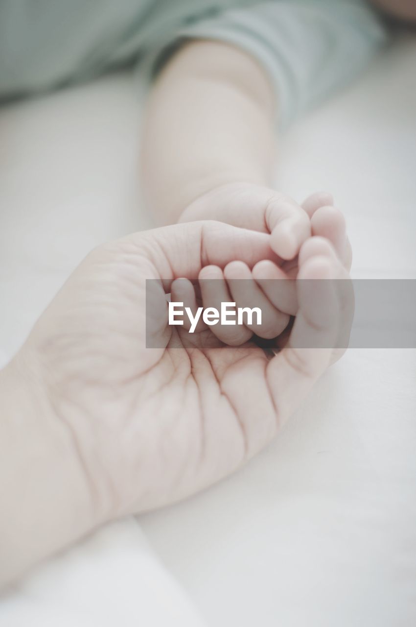 Cropped hand of mother with baby on bed