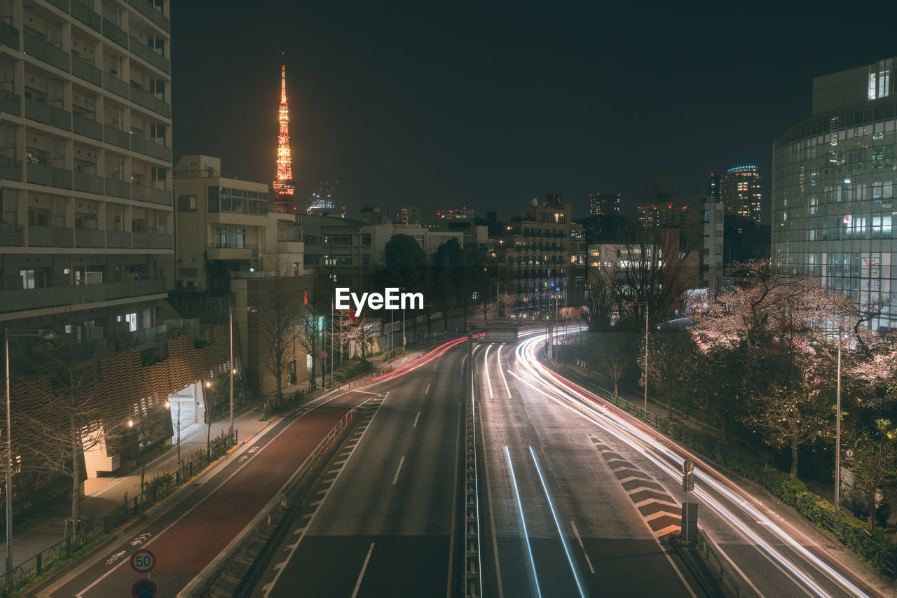 LIGHT TRAILS ON CITY STREET AMIDST BUILDINGS AT NIGHT