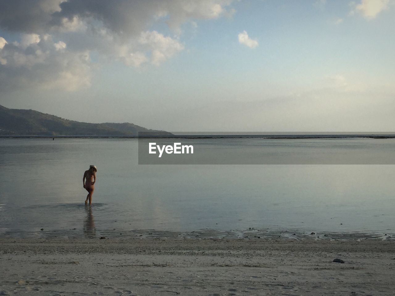 Rear view of sensuous woman walking in sea against sky