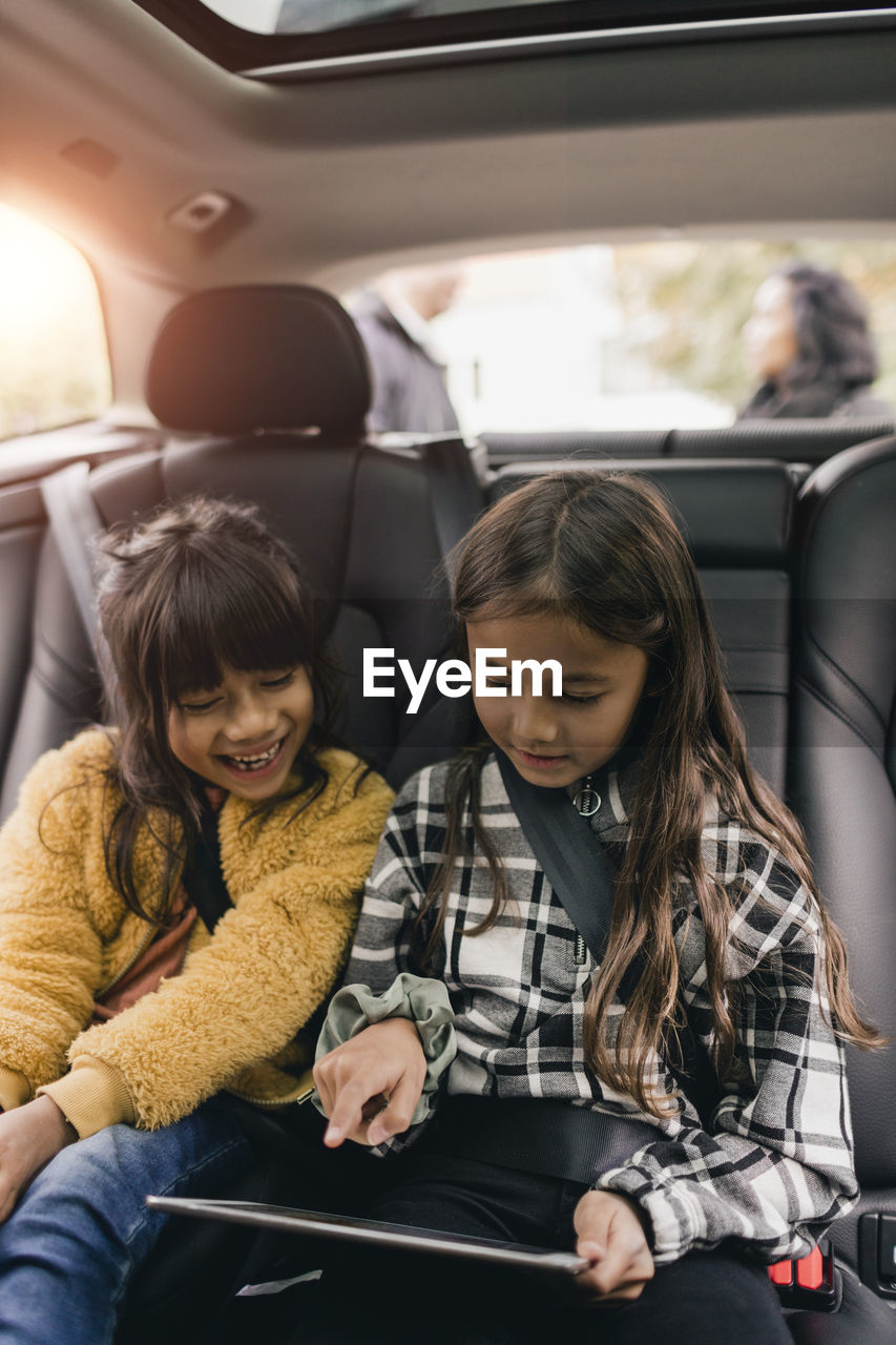 Sisters using digital tablet while sitting in car