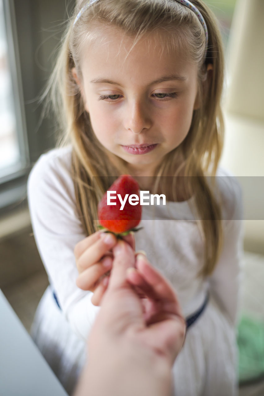 Cropped hand giving strawberry to girl