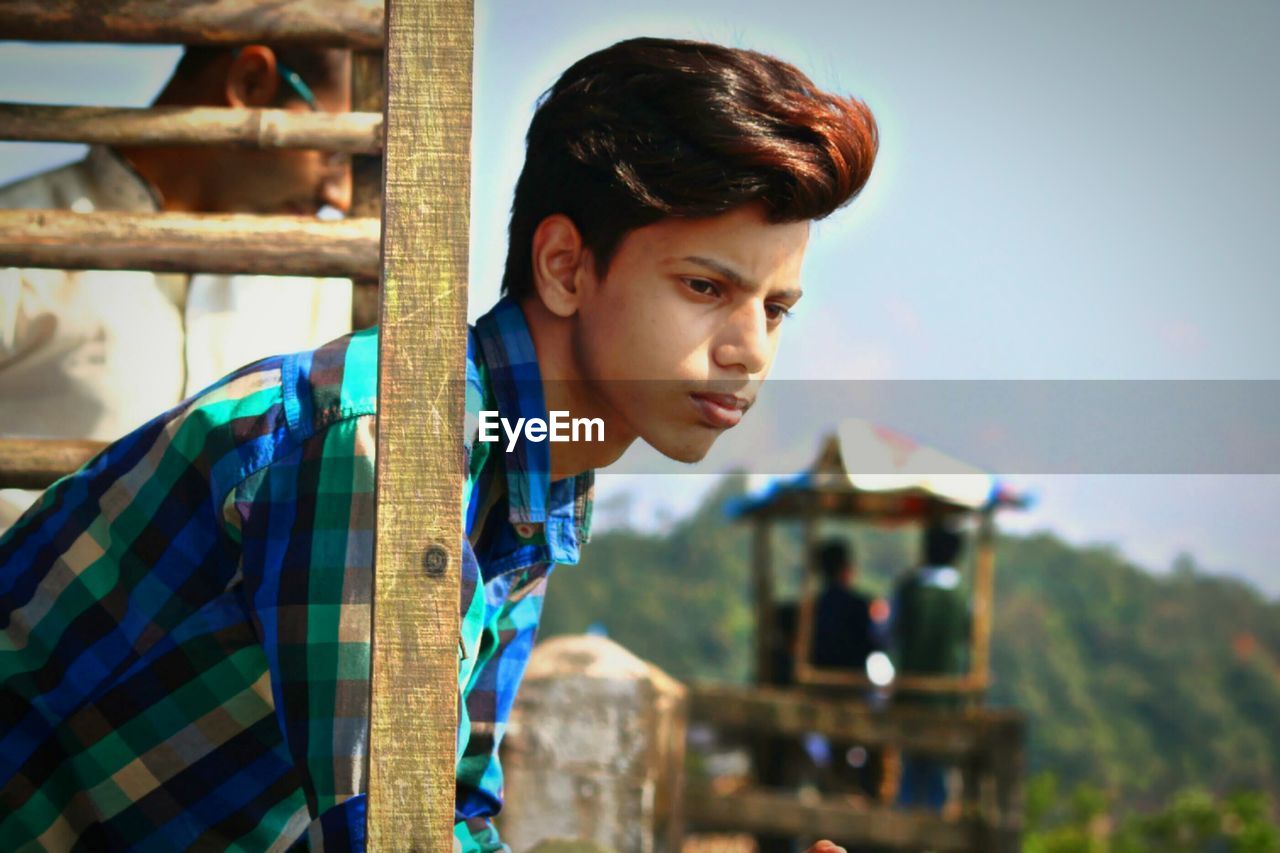 Young man looking away by sky
