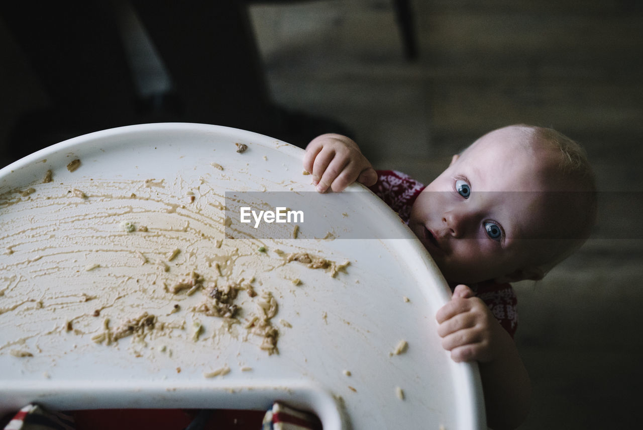 Portrait of toddler holding high chair with leftovers on it