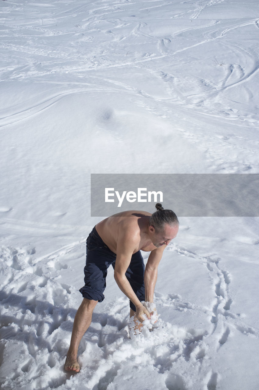 Adult man practicing cryotherapy, in the snow. cryotherapy is a pain treatment that uses a method
