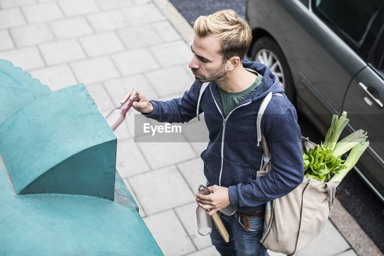 High angle view of man putting bottle in recycling bin