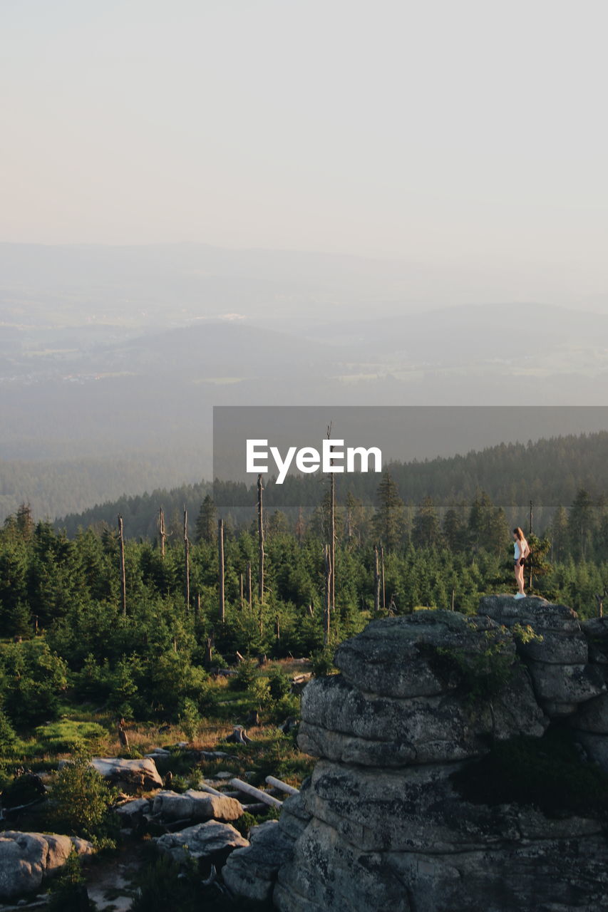 Scenic view of landscape with woman standing on rock against sky