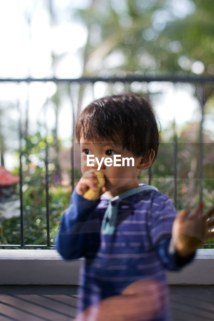 Cute boy eating food while looking away on balcony