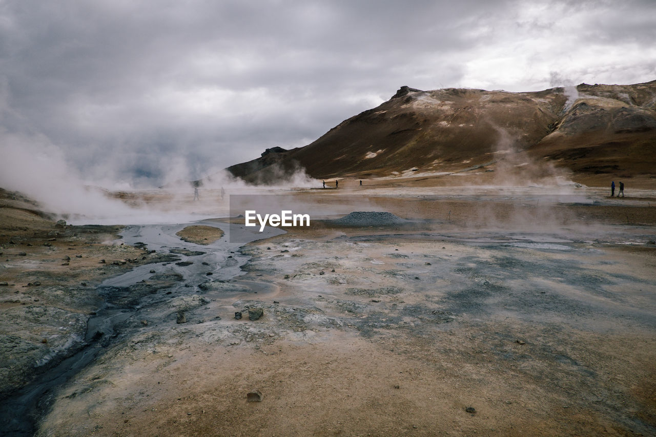 Steam emitting from geyser against cloudy sky