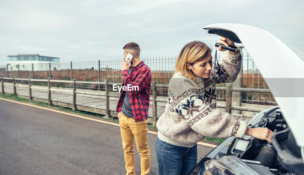 Woman repairing car while man talking on phone