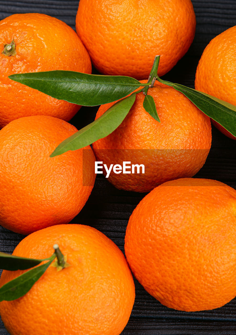 High angel view of whole ripe fresh citrus fruits tangerines with green leaves on black background.