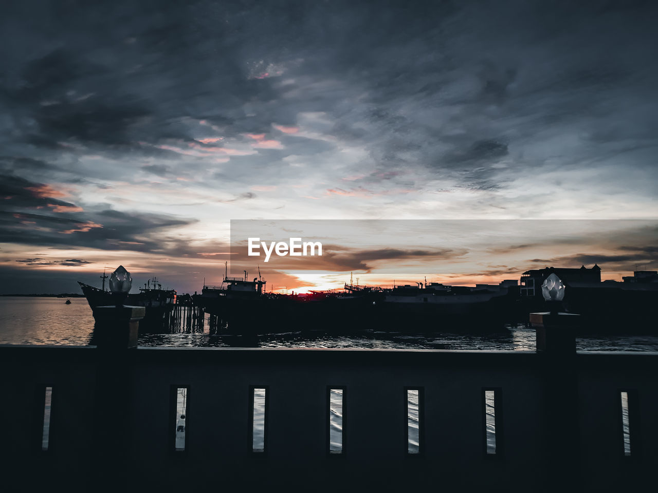 Silhouette city by river against sky at sunset